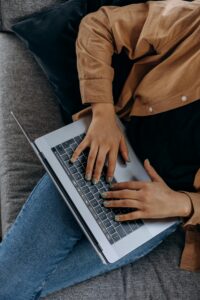 Home A person typing on a laptop while seated on a couch with casual attire, perfect for remote work imagery.